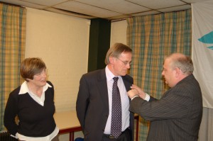 Albert Janssen krijgt onderscheiding van Jan Hilverts. Albert's vrouw kijkt toe.